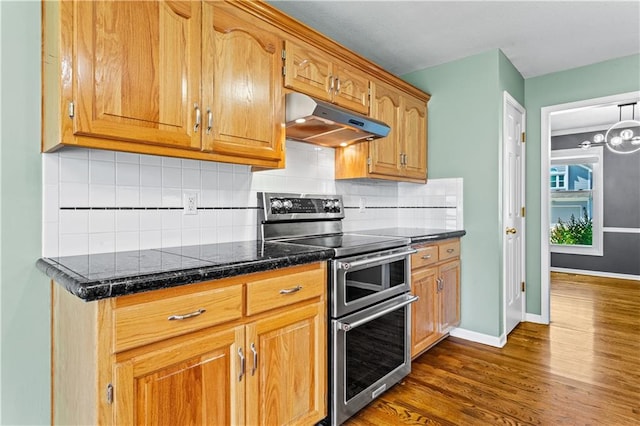 1321 SW Crossing Dr, Lees Summit, MO 64081 - kitchen with double oven range, under cabinet range hood, dark wood finished floors, dark stone countertops, and tasteful backsplash