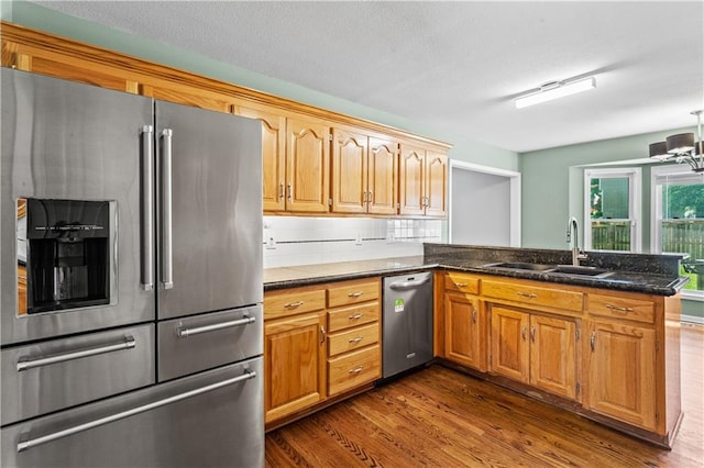 1321 SW Crossing Dr, Lees Summit, MO 64081 - kitchen with stainless steel appliances, dark wood-type flooring, a peninsula, dark stone counters, and brown cabinetry