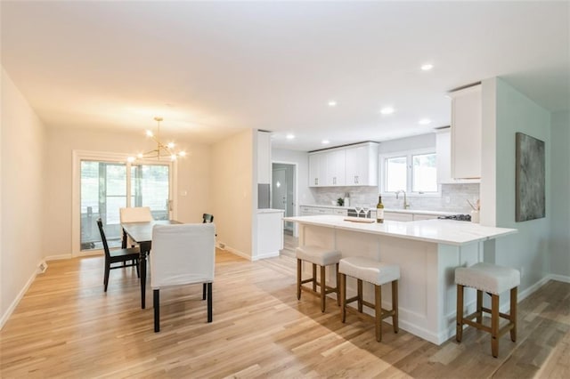 5308 Foster St, Mission, KS 66202 - kitchen featuring a breakfast bar, a chandelier, light wood-type flooring, tasteful backsplash, and white cabinetry