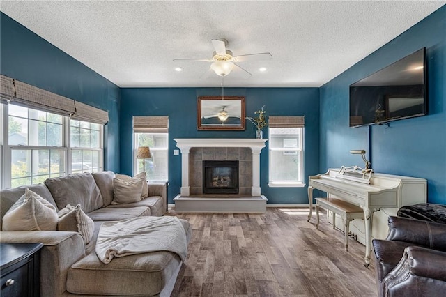 1210 NW Persimmon Dr, Grain Valley, MO 64029 - living room with ceiling fan, a textured ceiling, healthy amount of natural light, wood finished floors, and a tiled fireplace