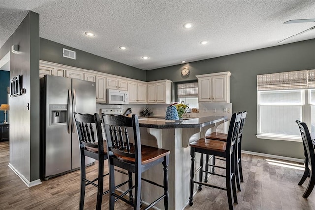 1210 NW Persimmon Dr, Grain Valley, MO 64029 - kitchen with stainless steel fridge with ice dispenser, white microwave, wood finished floors, a kitchen breakfast bar, and a textured ceiling