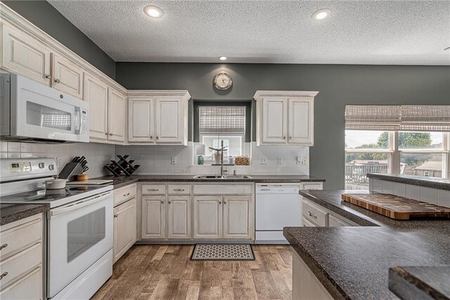 1210 NW Persimmon Dr, Grain Valley, MO 64029 - kitchen featuring white appliances, dark countertops, a textured ceiling, light wood-style floors, and tasteful backsplash