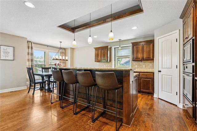 18501 S Butternut St W, Gardner, KS 66030 - kitchen featuring a breakfast bar area, appliances with stainless steel finishes, a textured ceiling, dark wood-type flooring, and decorative backsplash