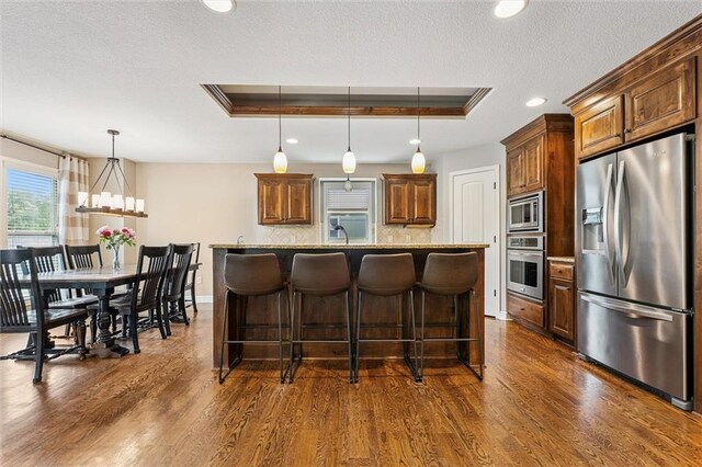 18501 S Butternut St W, Gardner, KS 66030 - kitchen with stainless steel appliances, a raised ceiling, a textured ceiling, dark wood-style flooring, and a kitchen bar