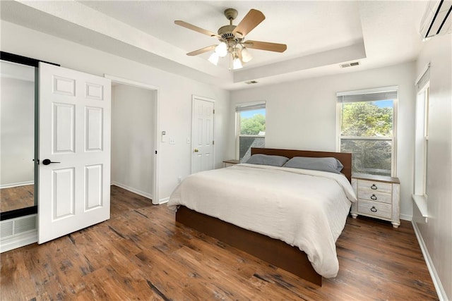 14733 Hickory Dr, Bonner Springs, KS 66012 - bedroom featuring a wall unit AC, a tray ceiling, wood finished floors, and a ceiling fan