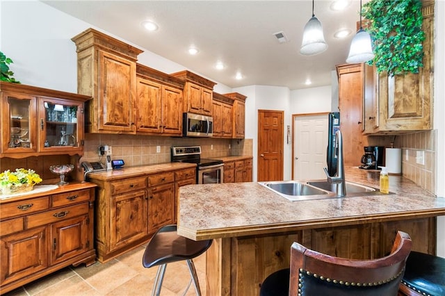 903 Howenstein St, Cameron, MO 64429 - kitchen featuring appliances with stainless steel finishes, brown cabinetry, a breakfast bar, a peninsula, and tasteful backsplash