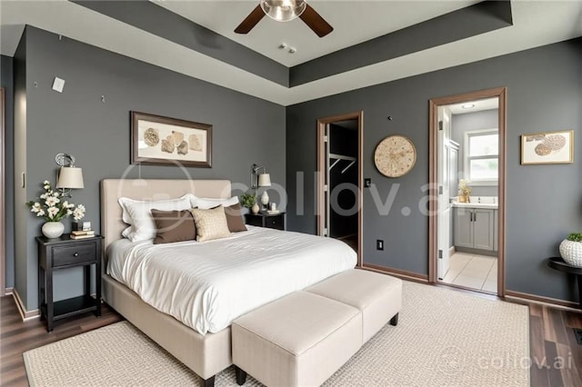 1039 Woodson Cir, Gardner, KS 66030 - bedroom with wood finished floors, a spacious closet, a tray ceiling, connected bathroom, and ceiling fan