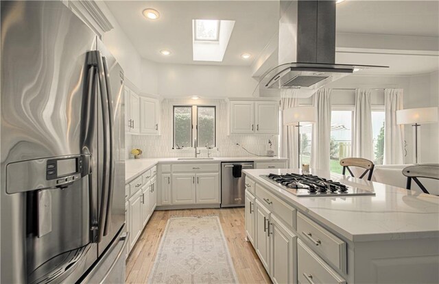 12600 Mohawk Ln, Leawood, KS 66209 - kitchen featuring appliances with stainless steel finishes, island exhaust hood, a skylight, light wood finished floors, and white cabinetry