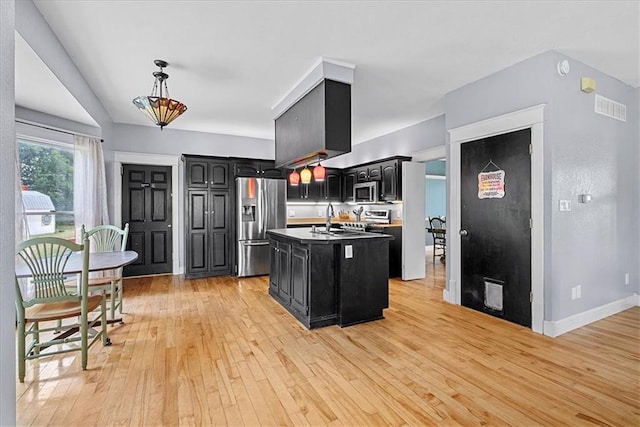 1148 N 1st Rd, Baldwin City, KS 66006 - kitchen with stainless steel appliances, dark cabinetry, light wood-style flooring, an island with sink, and hanging light fixtures