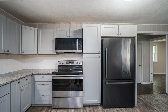 914 Jersey St, Baldwin City, KS 66006 - kitchen with appliances with stainless steel finishes, dark wood-style floors, a textured ceiling, light stone counters, and backsplash