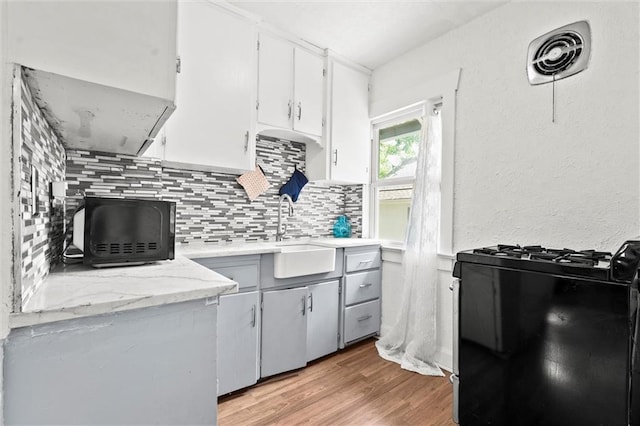 707 W 75th Ter, Kansas City, MO 64114 - kitchen featuring black appliances, light wood-type flooring, backsplash, a wood stove, and white cabinetry