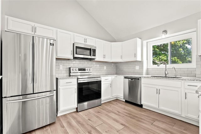 1108 W Pleasant Dr, Raymore, MO 64083 - kitchen featuring appliances with stainless steel finishes, white cabinets, lofted ceiling, light stone counters, and decorative backsplash