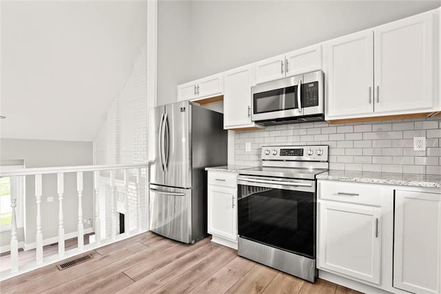 1108 W Pleasant Dr, Raymore, MO 64083 - kitchen featuring appliances with stainless steel finishes, white cabinetry, tasteful backsplash, light stone counters, and lofted ceiling