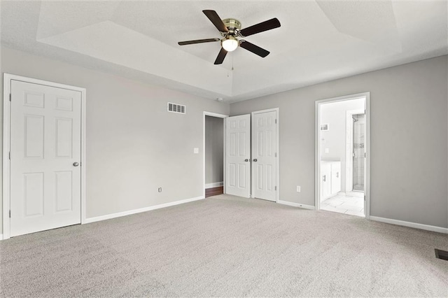 1108 W Pleasant Dr, Raymore, MO 64083 - unfurnished bedroom with a tray ceiling, carpet, ensuite bathroom, and ceiling fan