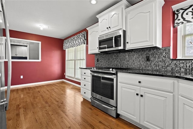 1002 W Howard Pl, Louisburg, KS 66053 - kitchen with appliances with stainless steel finishes, dark countertops, wood finished floors, white cabinetry, and decorative backsplash