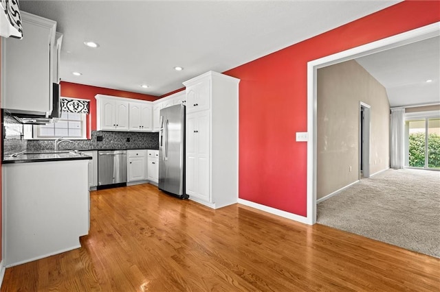 1002 W Howard Pl, Louisburg, KS 66053 - kitchen with stainless steel appliances, dark countertops, white cabinets, light wood-style flooring, and tasteful backsplash