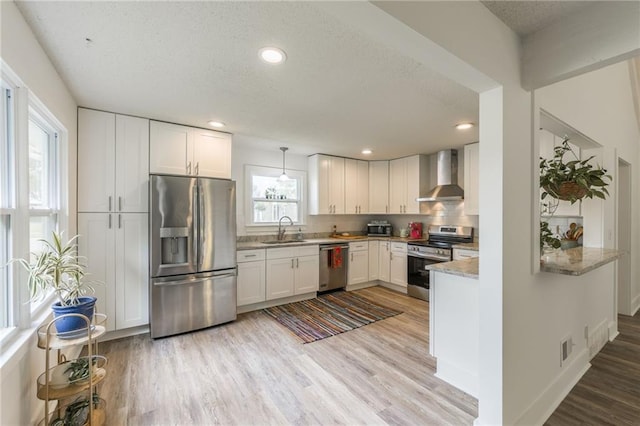 6613 E 123rd Ter, Grandview, MO 64030 - kitchen with stainless steel appliances, wall chimney exhaust hood, light wood-type flooring, white cabinetry, and decorative backsplash