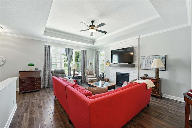 704 E 110th Ter, Kansas City, MO 64131 - living room featuring a tray ceiling, ceiling fan, a fireplace, dark wood-style floors, and ornamental molding