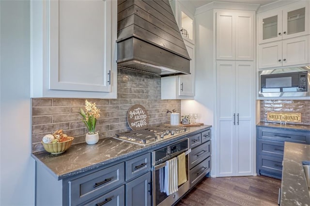 15389 W 173rd Ter, Olathe, KS 66062 - kitchen featuring appliances with stainless steel finishes, custom exhaust hood, white cabinetry, dark stone counters, and dark wood-style floors