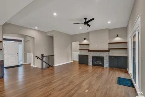 25446 W 91st Ter, Lenexa, KS 66227 - unfurnished living room featuring ceiling fan, wood finished floors, a stone fireplace, recessed lighting, and arched walkways
