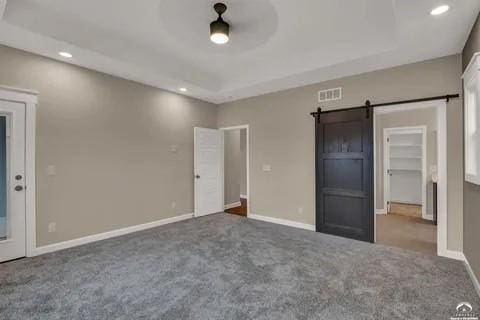 25446 W 91st Ter, Lenexa, KS 66227 - unfurnished bedroom featuring a barn door, carpet floors, recessed lighting, a raised ceiling, and a walk in closet