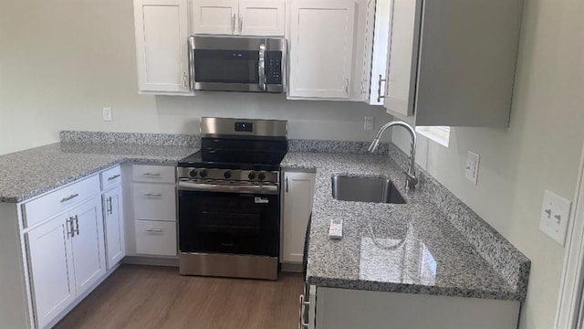 1106 S Mitchell St, Warrensburg, MO 64093 - kitchen featuring appliances with stainless steel finishes, white cabinets, wood finished floors, light stone countertops, and a peninsula