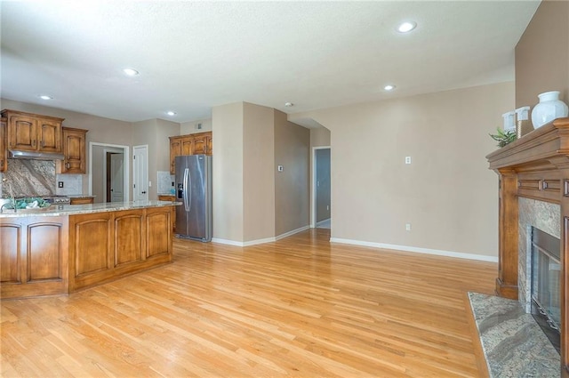 12337 Gillette St, Overland Park, KS 66213 - kitchen featuring stainless steel refrigerator with ice dispenser, under cabinet range hood, light wood-style flooring, brown cabinetry, and a high end fireplace