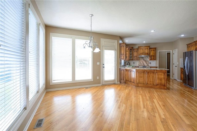 12337 Gillette St, Overland Park, KS 66213 - kitchen featuring stainless steel fridge with ice dispenser, brown cabinets, a peninsula, a chandelier, and light wood-style flooring