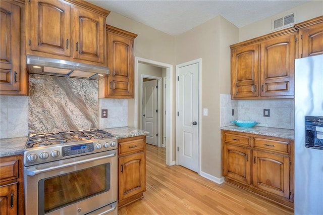 12337 Gillette St, Overland Park, KS 66213 - kitchen with stainless steel gas range, fridge with ice dispenser, under cabinet range hood, and brown cabinetry
