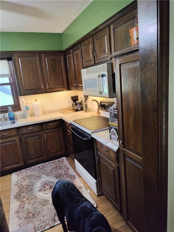 505 E Harold St, Olathe, KS 66061 - kitchen with white microwave, black range with electric stovetop, dark brown cabinetry, light countertops, and light wood-style floors