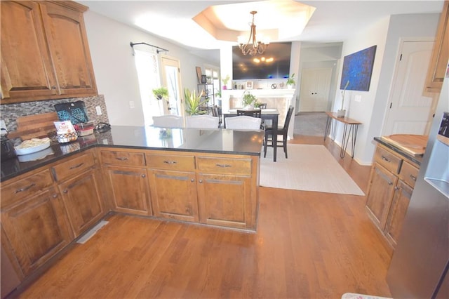 1207 SW 9th St, Oak Grove, MO 64075 - kitchen featuring brown cabinetry, a peninsula, a chandelier, light wood finished floors, and dark countertops