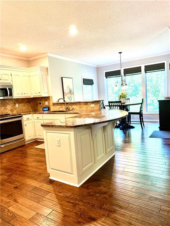 4531 Anderson St, Shawnee, KS 66226 - kitchen featuring stainless steel appliances, dark wood-style floors, crown molding, a textured ceiling, and a kitchen breakfast bar