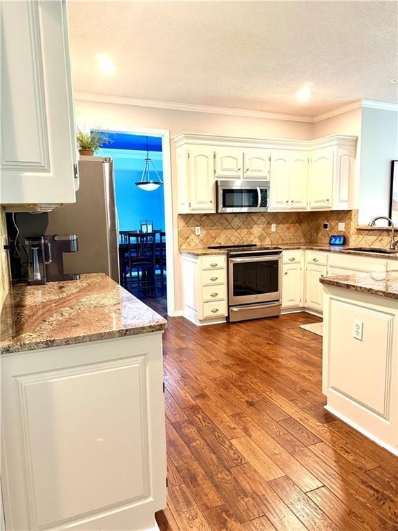 4531 Anderson St, Shawnee, KS 66226 - kitchen featuring appliances with stainless steel finishes, crown molding, light stone countertops, dark wood finished floors, and tasteful backsplash