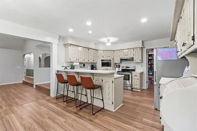 1803 N Jeter Rd, Raymore, MO 64083 - kitchen with stainless steel appliances, a kitchen breakfast bar, light wood-type flooring, light countertops, and a peninsula