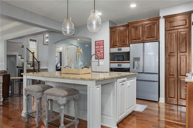 9445 W 157th Pl, Overland Park, KS 66221 - kitchen featuring fridge with ice dispenser, wood finished floors, arched walkways, a kitchen bar, and light stone countertops