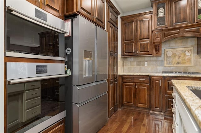 9445 W 157th Pl, Overland Park, KS 66221 - kitchen with stainless steel appliances, tasteful backsplash, dark wood finished floors, light stone counters, and glass insert cabinets