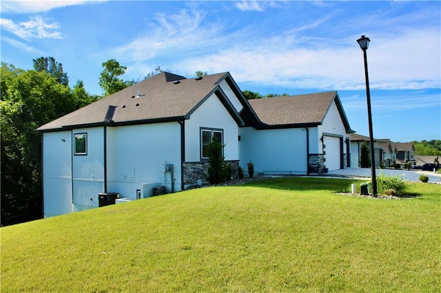 5443 N 101st Ter, Kansas City, KS 66109 - rear view of house with an attached garage, a lawn, concrete driveway, stone siding, and a shingled roof