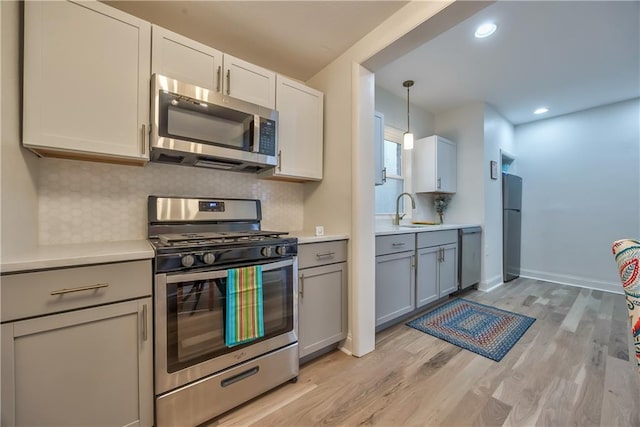 2606 Smart Ave, Kansas City, MO 64124 - kitchen with appliances with stainless steel finishes, light wood finished floors, light countertops, backsplash, and gray cabinets