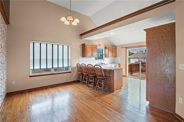 913 N Cochise Ave, Independence, MO 64056 - kitchen featuring vaulted ceiling, a chandelier, a kitchen breakfast bar, light wood finished floors, and a peninsula
