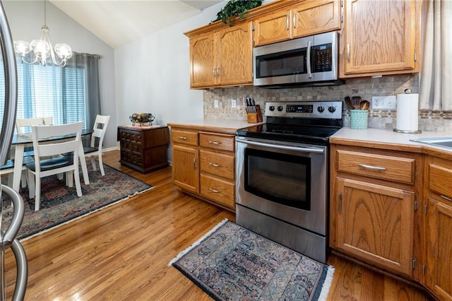 207 Woodhaven Dr, Smithville, MO 64089 - kitchen featuring stainless steel appliances, lofted ceiling, a chandelier, tasteful backsplash, and light wood finished floors