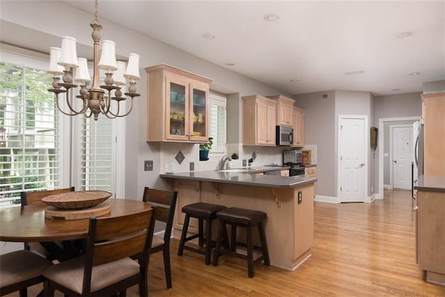 14333 Norwood St, Leawood, KS 66224 - kitchen with stainless steel microwave, a chandelier, light wood-type flooring, glass insert cabinets, and a breakfast bar area