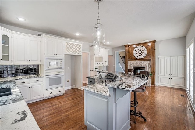 5713 NE Sapphire Ct, Lees Summit, MO 64064 - kitchen featuring white appliances, light stone countertops, a kitchen bar, white cabinets, and dark wood-type flooring
