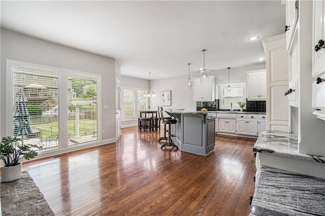 5713 NE Sapphire Ct, Lees Summit, MO 64064 - kitchen featuring a breakfast bar area, dark wood-style flooring, white cabinets, a chandelier, and a kitchen island