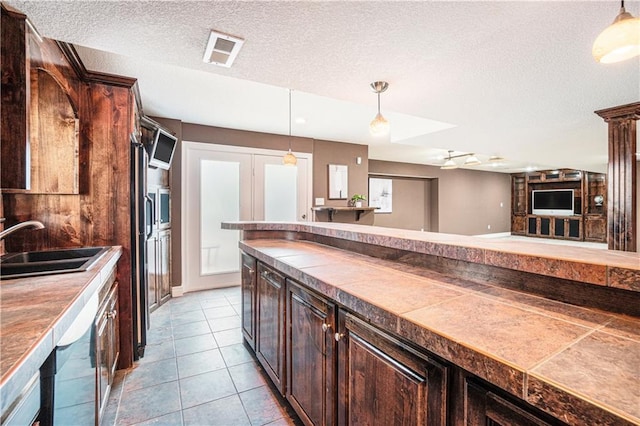 5713 NE Sapphire Ct, Lees Summit, MO 64064 - kitchen featuring dark brown cabinetry, a textured ceiling, decorative light fixtures, tile patterned flooring, and dishwashing machine
