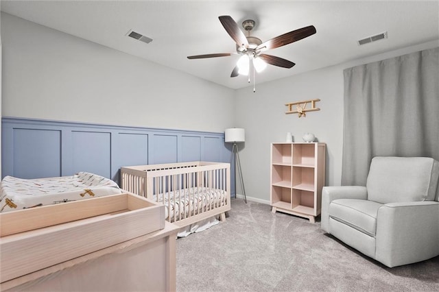 2312 SW Morris Dr, Lees Summit, MO 64082 - bedroom featuring light carpet, a nursery area, wainscoting, a decorative wall, and a ceiling fan