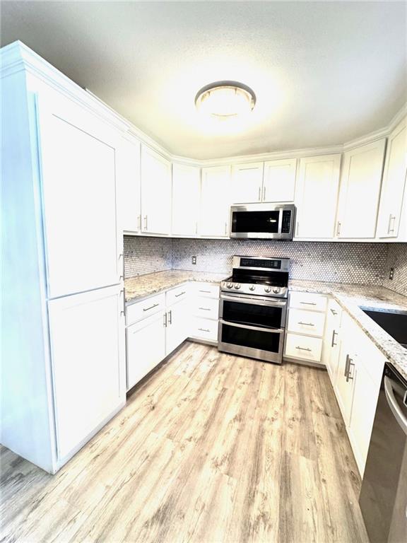 1012 NW A St, Blue Springs, MO 64015 - kitchen featuring appliances with stainless steel finishes, light wood-style flooring, light stone counters, and white cabinetry