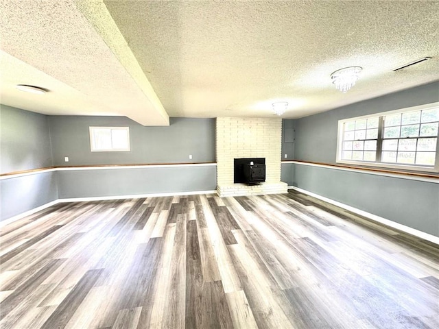 1012 NW A St, Blue Springs, MO 64015 - unfurnished living room featuring healthy amount of natural light, wood finished floors, a textured ceiling, and a brick fireplace