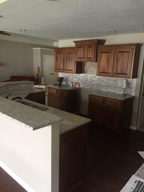 19706 E 20th St N, Independence, MO 64058 - kitchen with backsplash, a textured ceiling, light stone countertops, brown cabinetry, and dark wood finished floors
