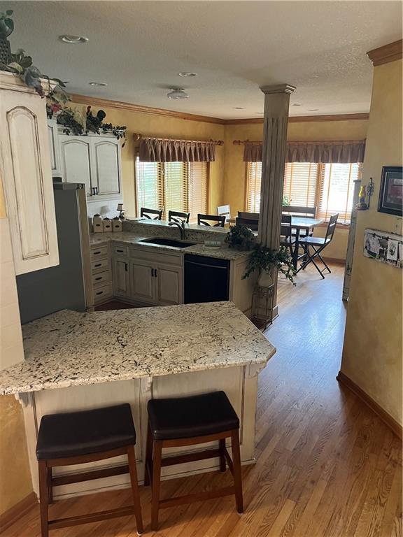 15733 Pine Cir, Basehor, KS 66007 - kitchen featuring a peninsula, black dishwasher, light wood-style floors, ornamental molding, and light stone countertops