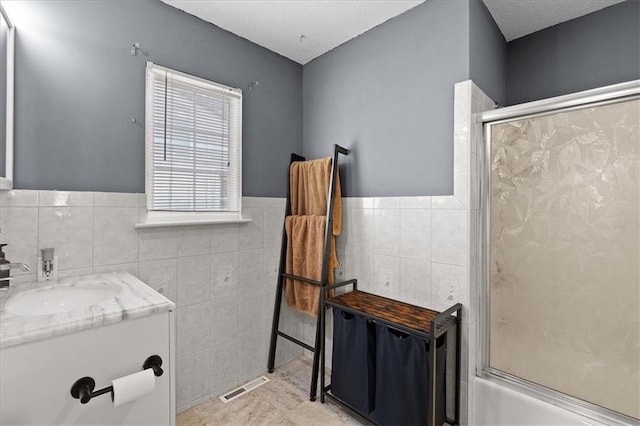 9410 Taylor Dr, Overland Park, KS 66212 - full bath with tile walls, vanity, shower / bath combination with glass door, wainscoting, and a textured ceiling